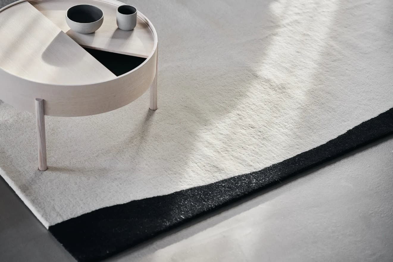 Der Flow Wollteppich weiß-schwarz von Scandi Living ist ein handgetufteter Teppich mit einem weiß Untergrund und zwei organisch geformten Blöcken in einer kontrastierenden schwarzen Farbe