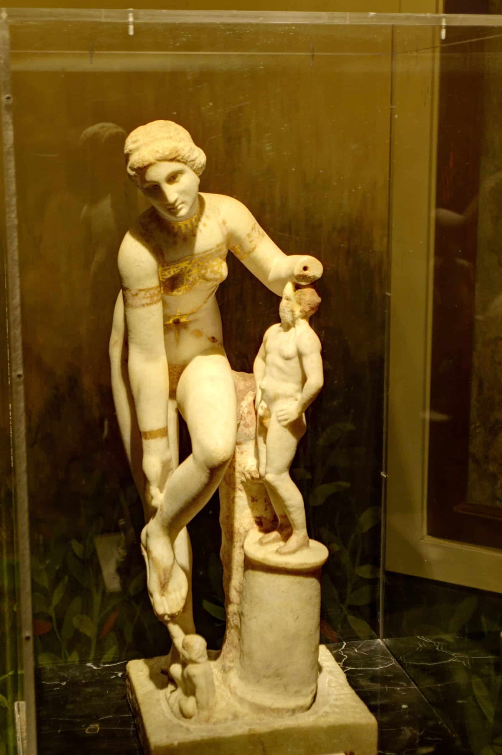 Die sogenannte „Venus im Bikini“, einer mehrfarbige römische Marmorstatue aus Pompeji (ca. 79 n. Chr.), stellt ihr griechisches Gegenstück Aphrodite dar, die bereit ist, ihre Sandale vor einem kleinen Eros zu lösen (Neapel, Archäologisches National Museum)