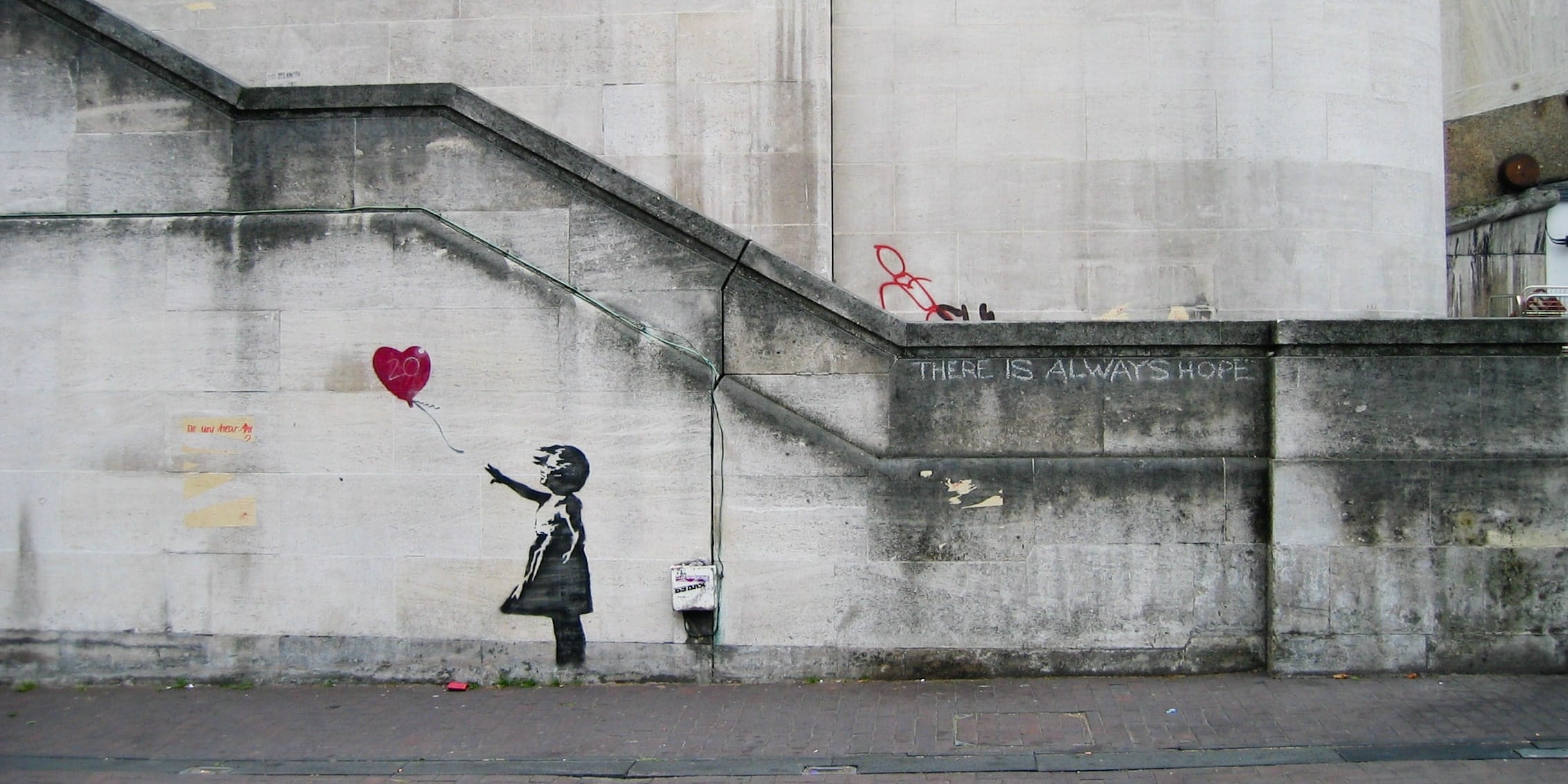 „Girl With Balloon“ (2004) ist Banksys berühmtestes Motiv. Es zeigt ein Mädchen, das nach einem herzförmigen Ballon im Banksy-Graffiti-Schablonenstil greift. Die Interpretation des Werks von Banksy ist subjektiv: Manche sehen darin ein Symbol des Verlusts, während andere Hoffnung und Freiheit darin finden.