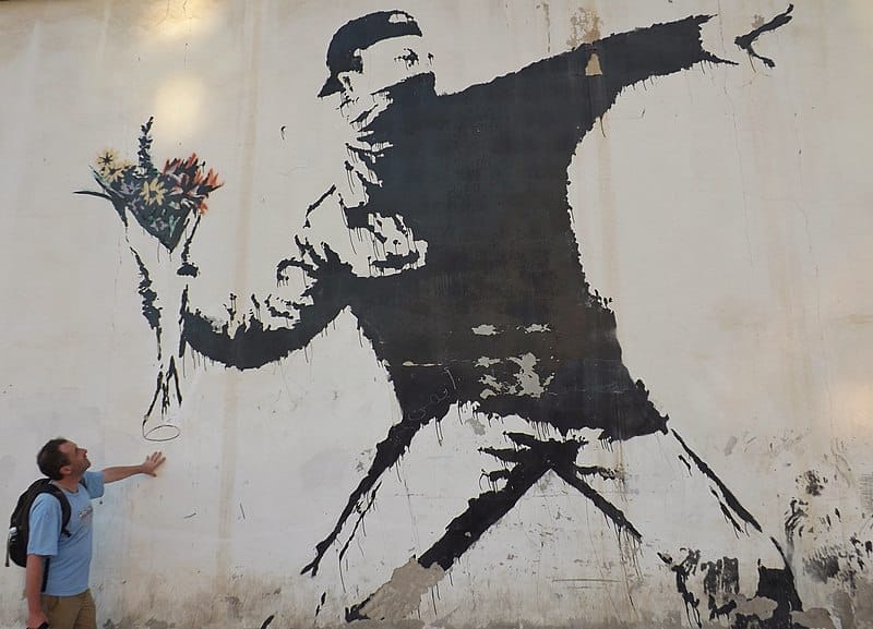 „Rage, the Flower Thrower“ oder „Love is in the Air“ ist eine der kultigsten Schablonen Murals von Banksy. Es zeigt einen maskierten Palästinenser, der einen Blumenstrauß wirft.