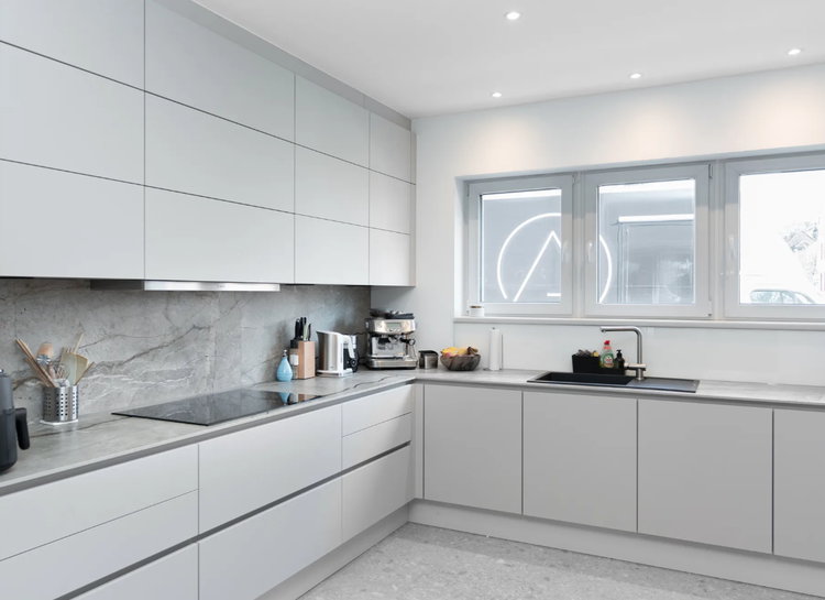 Die hellen, matten Fronten dieser Einbauküche sorgen für eine zeitlose Eleganz, während Arbeitsplatte und Rückwand in edler Steinoptik eine natürliche und luxuriöse Atmosphäre schaffen.