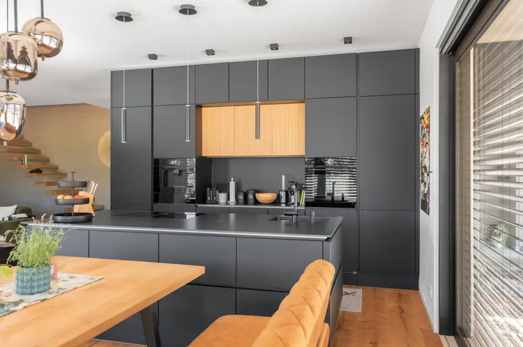 Diese stilvolle Designküche kombiniert matte, grifflose Fronten in Schwarz mit natürlichen Holzelementen und einer dezentralen Beleuchtungsvariante.