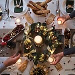 Die Weihnachtstafel als Stillleben: Was der Festtisch von der Malerei lernen kann Wanddeko 17. jahrhundert Festliche Tafel mit üppigem, mit Lichterketten und Goldkugeln geschmücktem grünen Kranz als strahlendem Herzstück. Zudem werden essbare Elemente wie liebevoll verzierte Lebkuchenhäuschen und verstreute rote Beeren charmant direkt in die Dekoration integriert, was für ein besonders einladendes, familiäres Ambiente sorgt.